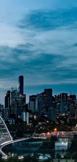 City skyline with bridge at dusk, lights glowing under a dark blue sky.