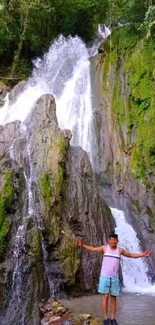 Man in front of a stunning waterfall in a lush green forest.