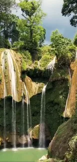 Lush green forest with cascading waterfall under a cloudy sky.