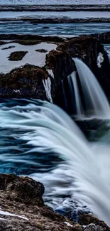 Beautiful waterfall cascading down rocky cliffs in a serene, snowy landscape.