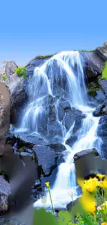 Vibrant waterfall over rocks with flowers and blue sky.