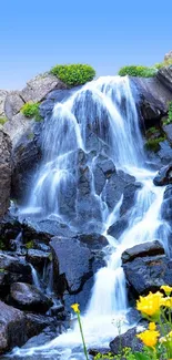 Refreshing waterfall with bright blue sky and yellow flowers.