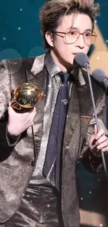 Stylish person in shiny suit holding a trophy with a blue backdrop.