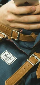 Close-up of a hand holding an iPhone over a stylish backpack with leather straps.