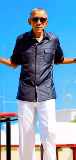 Man in navy shirt and white pants by the beach.