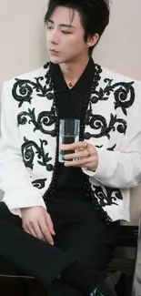 Man in black and white embroidered jacket holding glass.