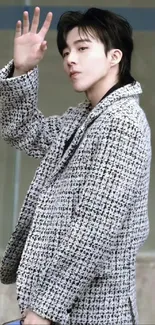 Stylish figure in a black and white patterned coat waving.