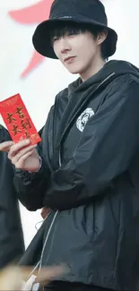 Person in a black jacket holding a red envelope.