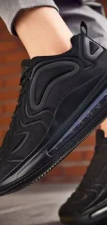 Black sneaker in front of a brick wall background.