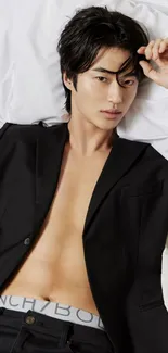 Model in black suit lying on a bed in modern fashion style.