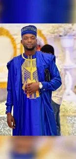 Man in vibrant blue traditional attire at a decorative venue.