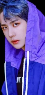 Person in a blue and purple hoodie against a dark background.