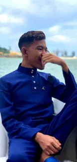 Man in blue outfit relaxing on a boat against a scenic lake background.