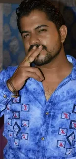 Man in a blue shirt posing confidently with a stylish backdrop.