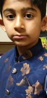 A young boy in a stylish blue floral jacket posing indoors.