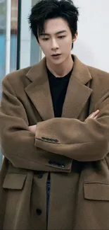 Stylish person in a brown coat posing against a modern backdrop.