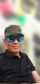 Man with camouflage cap and sunglasses in relaxed pose.