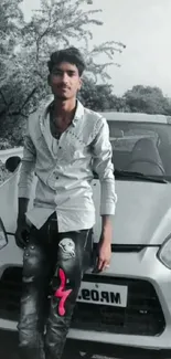 Young man posing with car in scenic grayscale setting.