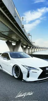 White sports car under a large bridge with a blue sky.