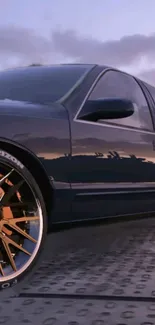 Sleek car with vibrant wheels on display at sunset.