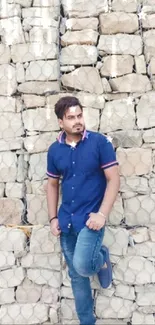 Man in blue shirt against stone wall background.