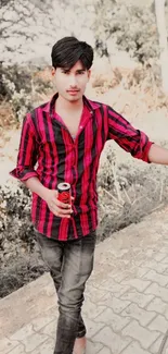 Young man in striped shirt outdoors with drink can.