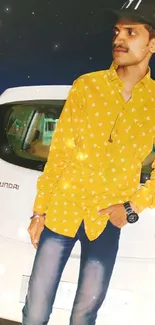 Man in yellow shirt leaning on a car at night.