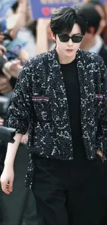 Stylish celebrity wearing a black sequin jacket surrounded by a crowd.