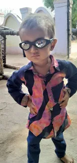 Child wearing sunglasses in a rustic village setting.