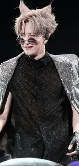 Performer in sparkling outfit with sunglasses on stage.