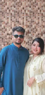 Couple in stylish traditional attire with a textured brick background.