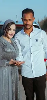 Stylish couple posing by car under clear blue sky.