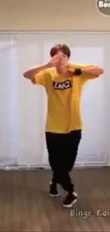 Dancer in yellow shirt performing in a room with wooden floor.