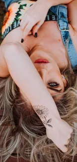 Woman in denim with tattoo on arm, lying on wooden deck.