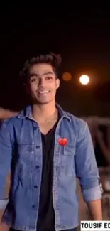 Young man in denim jacket with heart icon at night.