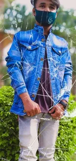 A person in a denim jacket poses outdoors amidst green foliage.