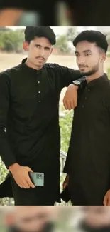 Two men in black traditional attire posing outdoors.