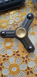 Black and gold fidget spinner on lace-patterned background.