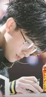 Person writing, wearing glasses, black hair, focused expression.