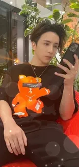 Man in black shirt with orange print sitting on red chair using smartphone.