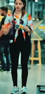 Person in colorful gym attire holds a bottle in modern fitness center.