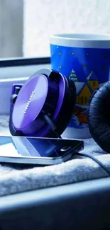 Purple headphones beside a smartphone and mug on a windowsill.