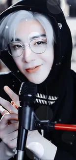 Singer in hoodie with glasses, holding a microphone.