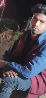 Person in blue and red jacket sitting outdoors at night.