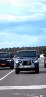 Three black Jeeps driving on an open highway under a clear blue sky.