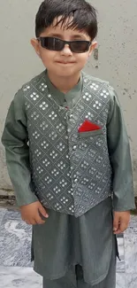 Young boy in green traditional outfit with sunglasses.