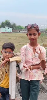 Two stylish kids posing outdoors with a rural backdrop.