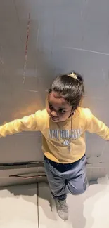 Child in yellow shirt posing with urban backdrop.