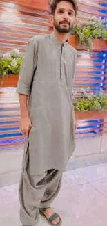 A person in a grey kurta with a blue and brown accent wall background.