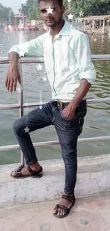 Man in casual attire posing by a scenic lakeside.